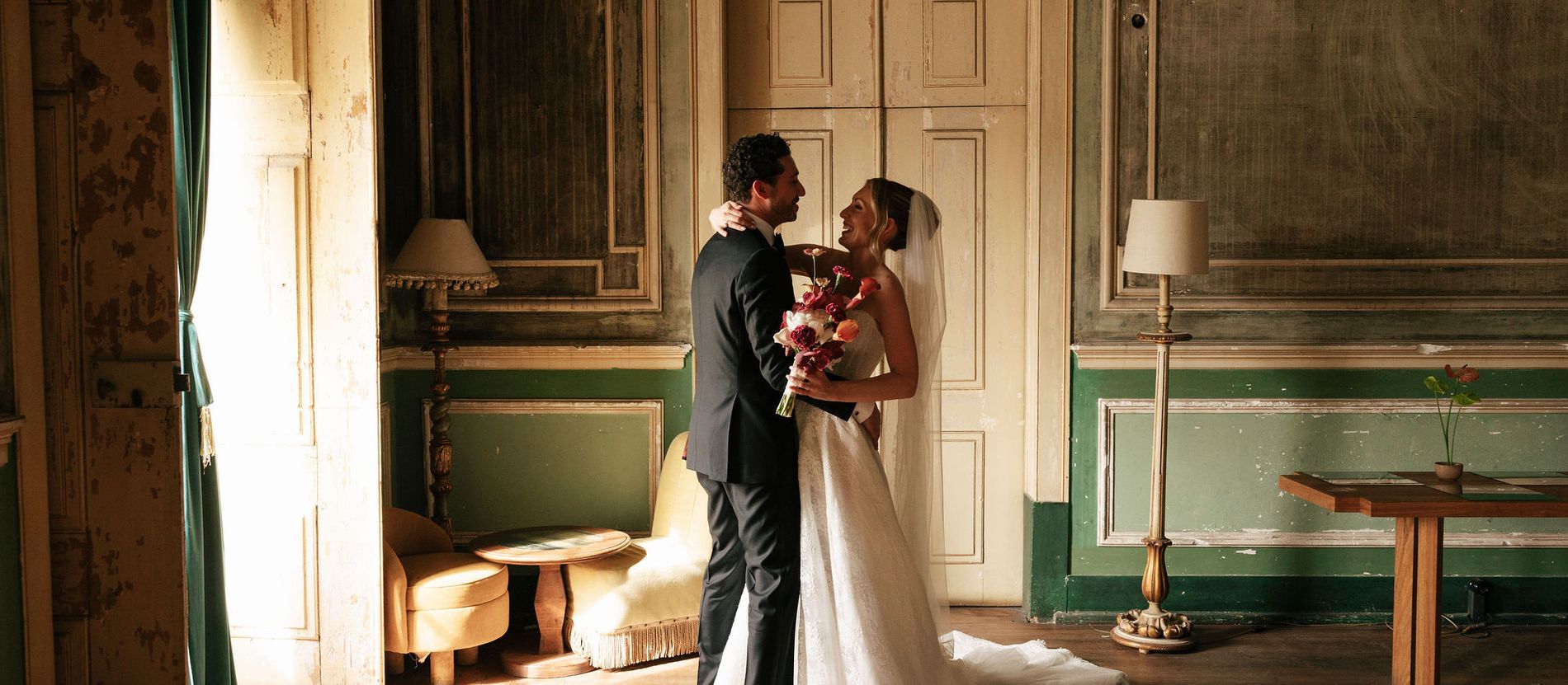 A bride and groom embracing in a faded, green-panelled room at a Portuguese palace