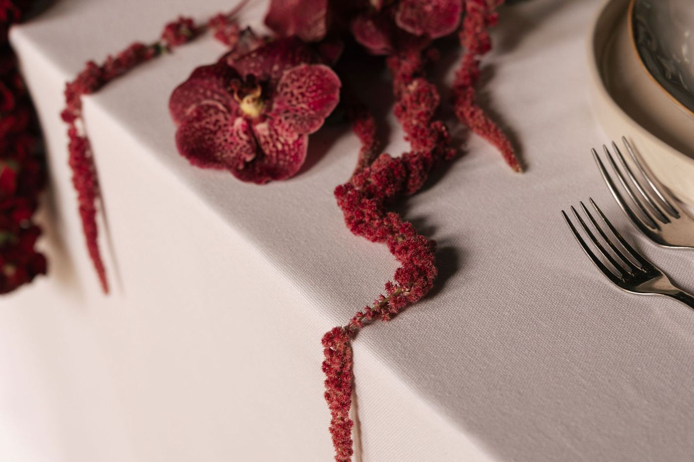 Burgundy orchids and amaranthus laid along the edge of a white linen table