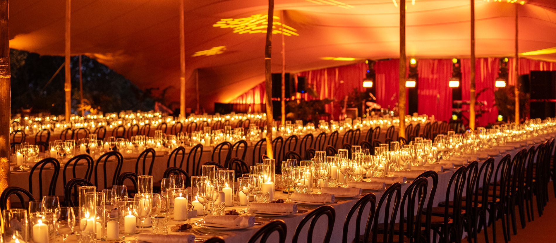 A candlelit marquee laid for dinner, long tables running away into the dark