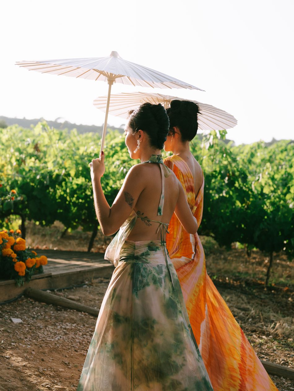 Two guests carrying paper parasols walking through a vineyard at sunset