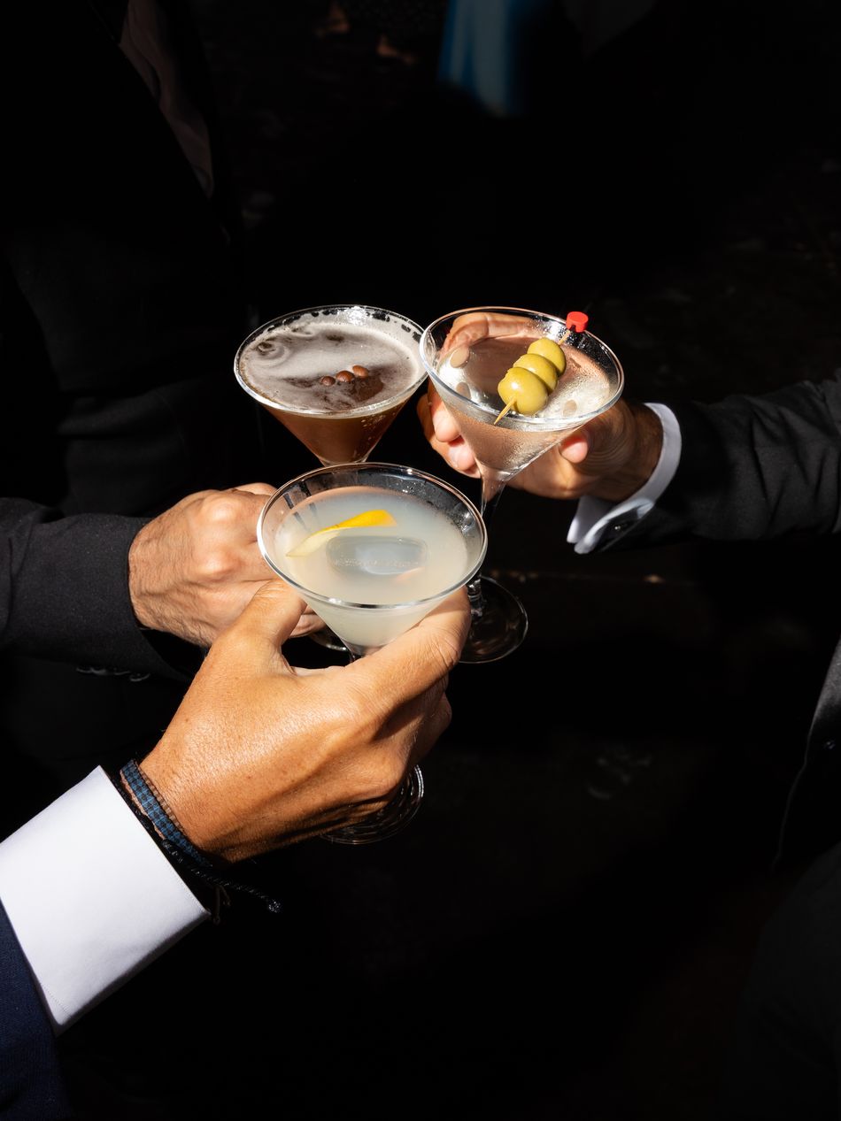 Three cocktails raised in a toast, guests in black tie