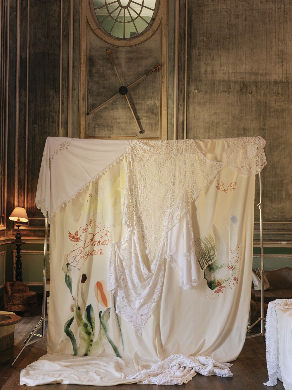 A hand-painted and embroidered cloth backdrop hung with antique lace in a faded palace room